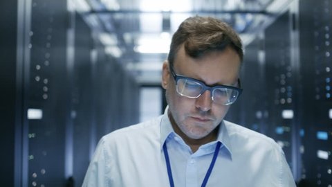 Follow-up Shot of IT Technician Walking Through Data Center. Rows of Working Server Racks are Visible and Have Blinking LED Lights. Shot on RED EPIC-W 8K Helium Cinema Camera.