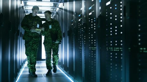 Two Military Men Walking in Data Center Corridor. One Uses Tablet Computer, They Have Discussion. Rows of Working Data Servers by their Sides. Shot on RED EPIC-W 8K Helium Cinema Camera.
