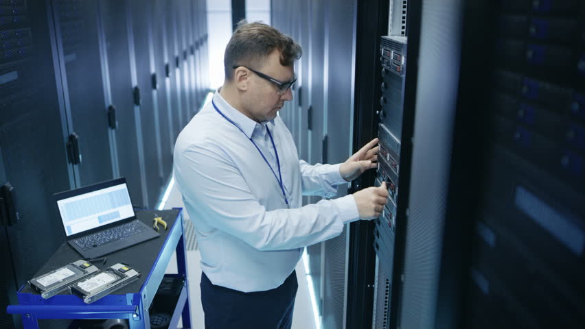 IT Engineer Taking Hard Drives off the Crash Cart and Installing Them into Rack Server. He's Working in Data Center. Also He Uses Laptop. Shot on RED EPIC-W 8K Helium Cinema Camera. | Shutterstock HD Video #26008058