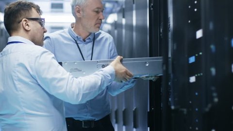 Two Server Technicians Install Hardware in Server Rack. They Work in Big Modern Data Center. Shot on RED EPIC-W 8K Helium Cinema Camera.