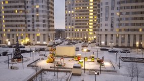 Winter yard of apartment complex with cars child playground and illuminated New Year tree in evening, mobile phone video.