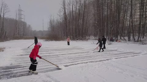 Four men, woman and girl clear ice of pond from snow near woman and child in park Losiny Ostrov, mobile phone video.