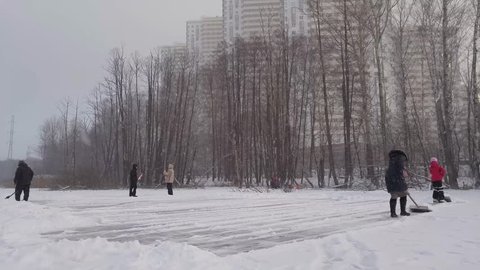Woman, girl and man clear ice of pond from snow near woman and man in park Losiny Ostrov, mobile phone video.