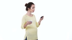 Smiling young pregnant woman shopping online with smartphone and credit card isolated over white
