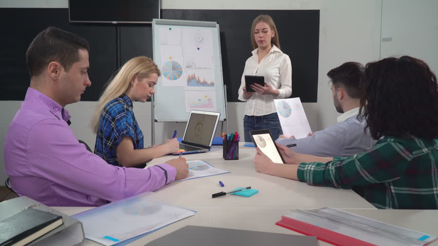 Young successful business team working in the office. Woman standing near flipchart using digital tablet tell about new products or services. Five professional workers in boardroom. Royalty-Free Stock Footage #26015036
