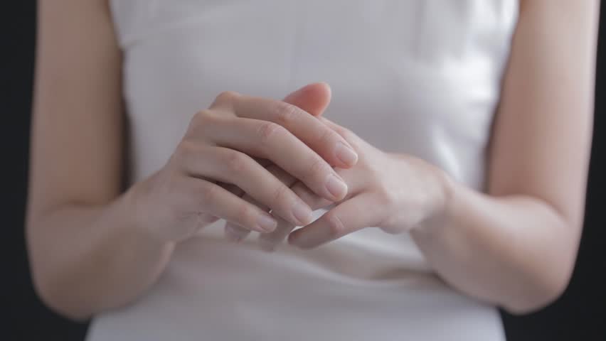 A woman in white shirt applying skin care cream or serum on her hand and arms. | Shutterstock HD Video #26018180