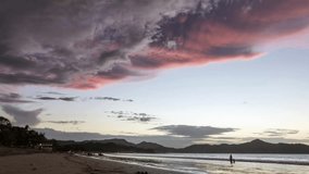 Timelapse of sunset on the beach of Brasilito, Tamarindo area, Costa Rica. Pink sky, low clouds, car driving on the beach in distance. 