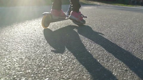 Little girl goes for ride on scooter at sunset. Tracking shot. slow motion