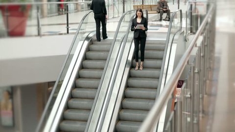 Young businesswoman talking at the phone on escalators. Business woman full lenght in shopping mall or office building or airport terminal.