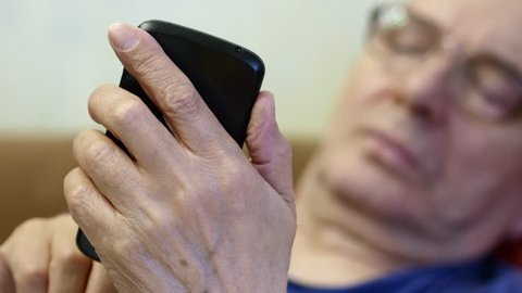 Elderly Man Using Smartphone Lying On The Couch