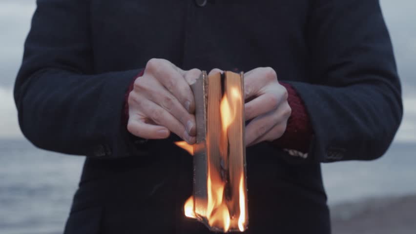 Young man dressed in gray coat with a burning book in hand standing on coast storm clouds on background strong bright flame surrealistic picture | Shutterstock HD Video #26028017