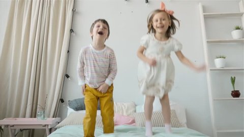 Portrait of children jumping on a bed, little boy and girl brother and sister have fun and laughing, happy kids on quarantine, coronavirus home isolation