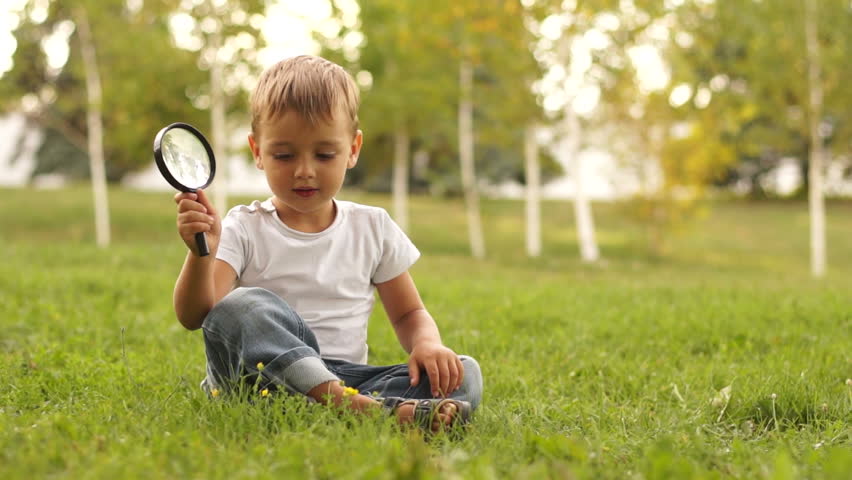 Boy looking at magnifier and sitting on the grass
