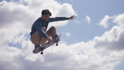 Skateboarder grabs his board in mid air during a jump, in slow motion