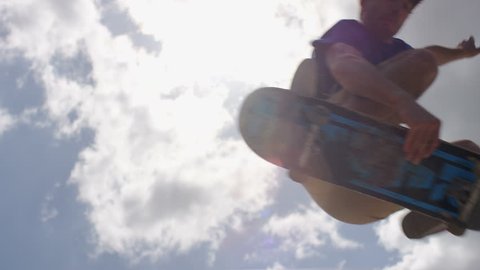 Close up of skateboarder doing an ollie jump against the clouds, in slow motion