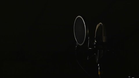 Microphone on a stand located in a music studio recording booth under low key light.
