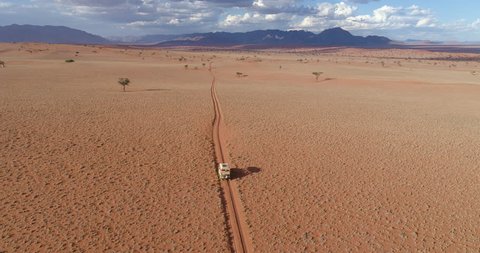 4K aerial view of safari vehicle driving on sand track road in the Namib desert