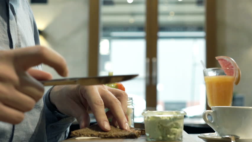 Man preparing and eating sandwich sitting in cafe
