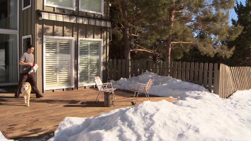 Man drinking coffee and reading the newspaper with golden retriever on front deck of home