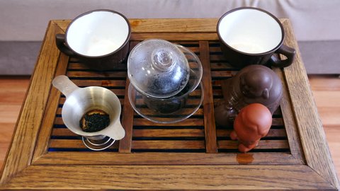The action of traditional Chinese tea ceremony. Pouring tea from covered bowl in a cup. Wooden tea board on the background.