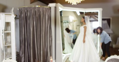 4k, Owner assisting young bride getting dressed in wedding gown. Slow motion. Champagne & flowers in foreground with designer assisting a young bride in background. Video de stock