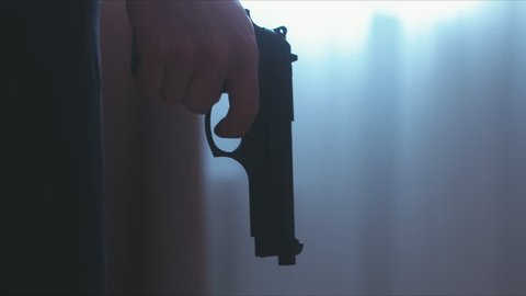 LR DOLLY Silhouette of male criminal pulling back the hammer of a pistol near the window. 4K UHD RAW edited footage
