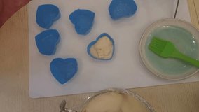 Woman hand pouring liquid dough in silicone molds in heart form on table close up, mobile phone video.