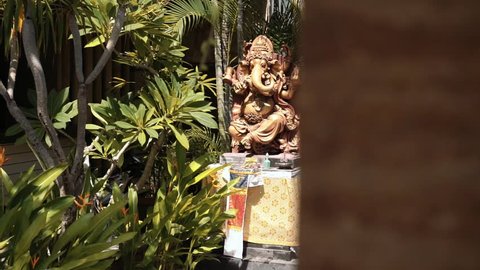 Big statue of hindu deity Ganesha with altar in front of a house, between trees