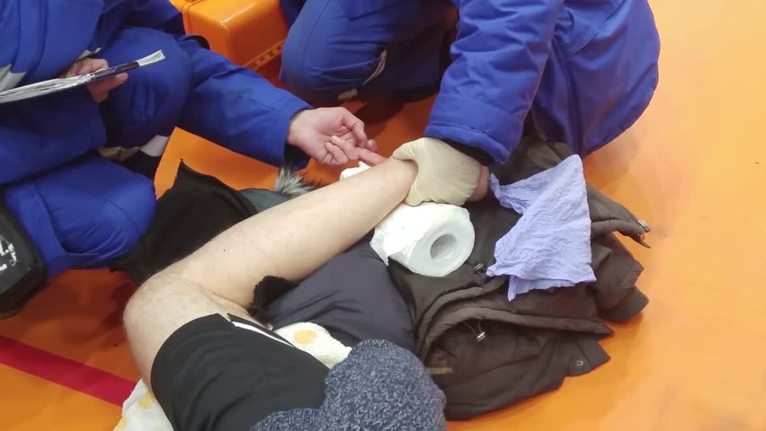Hands of first aid employees touching disjointed foot of man on volleyball square, mobile phone video.