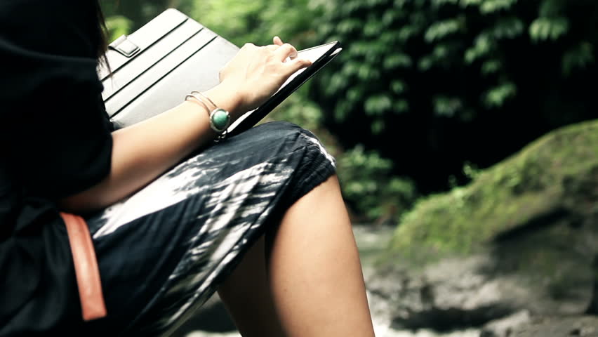 Young woman using a computer tablet in nature surrounding with rocks and river