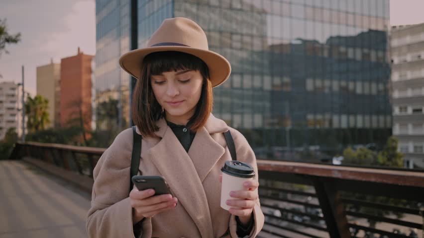 Trendy student in fedora hat, round glasses and hipster backpack scrolls through her news feed on smartphone on way to university college to stay up to date with events and social media Royalty-Free Stock Footage #26057549
