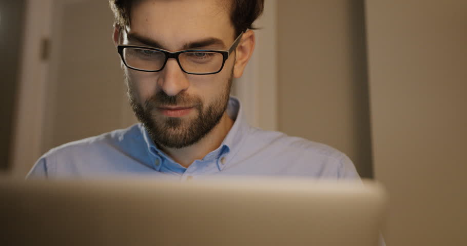 Beatiful man in glasses typing on his laptop. Business man working on office background. Close up.