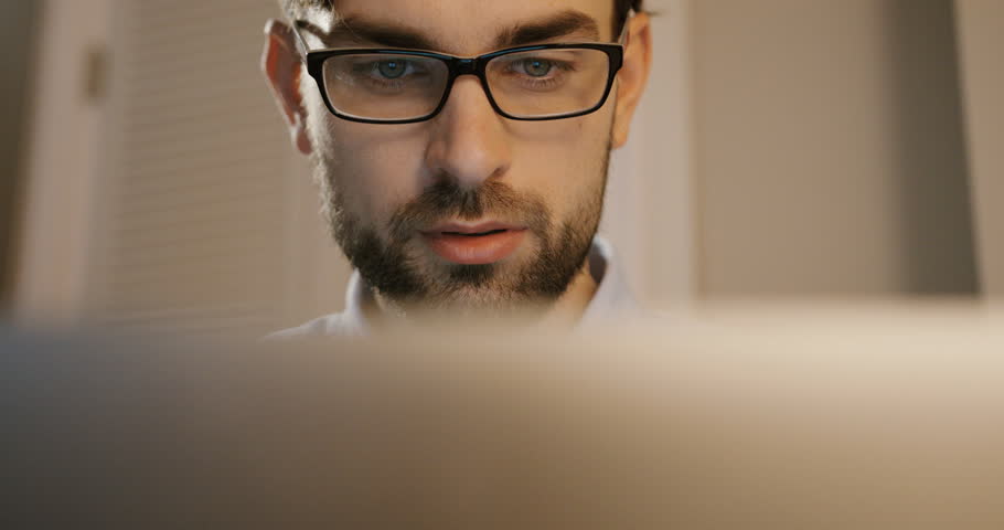 Attractive man in glasses typing on his laptop. Business man working on office background. Close up.