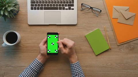 Man using smart phone with green screen on wooden table background. Male hands scrolling pages, zooming, tapping on touch screen. top view. Office stuff on desk background. Chroma key. Tracking motion Stock Video