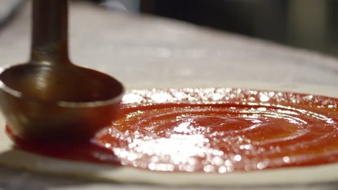 Tracking slow motion shot of applying tomato ketchup with metal ladle on pizza base
