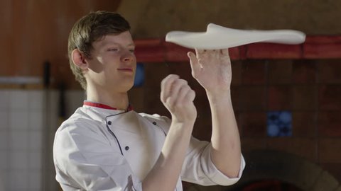Young pizzaiolo tossing pizza dough up in the air with two hands in restaurant kitchen