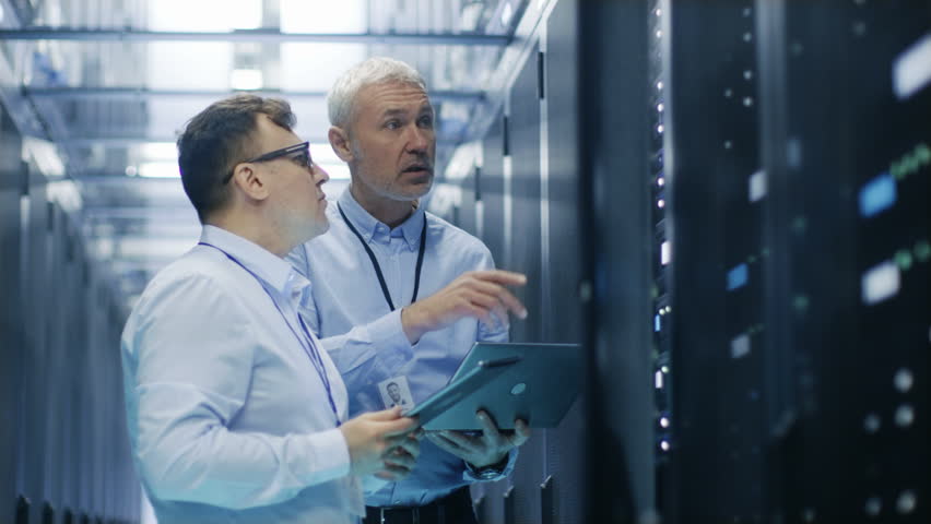  Two IT Technicians Standing in Data Center. They Use Laptop and Tablet Computer while Standing Beside Open Server Rack Cabinet.Shot on RED EPIC-W 8K Helium Cinema Camera. Royalty-Free Stock Footage #26069855