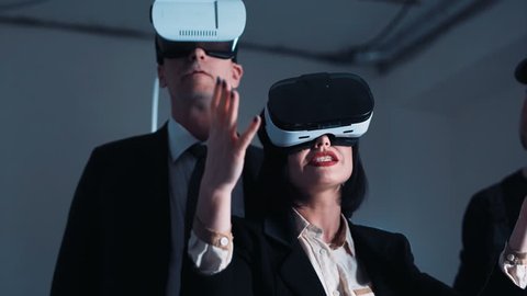 The people with virtual reality headsets on a construction site. The woman shows to group of architects and engineers the project of future interior of the room in the 3D simulator