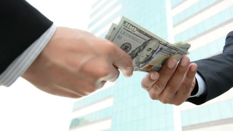 Businessman giving money, US dollar bills, to his partner