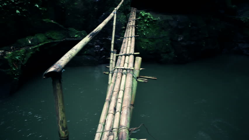A shaky walk over a bridge made from bamboo leading over a green river located