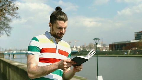 Handsome man in colorful shirt reading book on boulevards on sunny day
