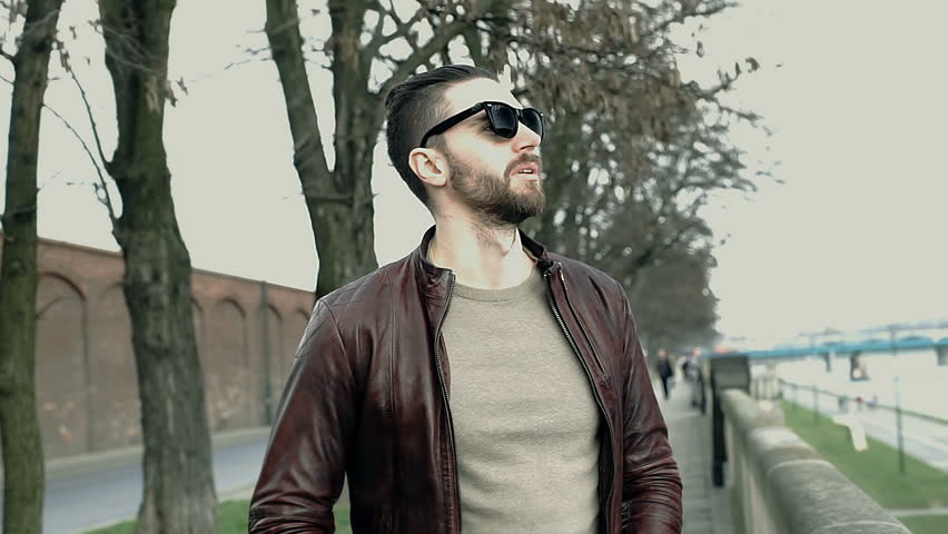 Stylish man in leather jacket standing on boulevards on windy day
