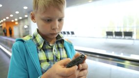 Closeup of child in terminal of airport and using smartphone. Focus at telephone. Age of little boy is 9 years old. Real time full hd video footage.
