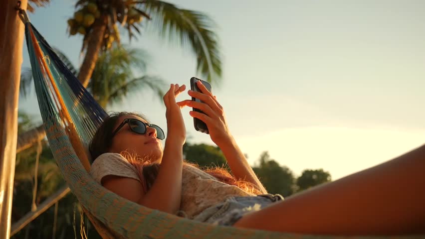 Relaxed Mixed Race Young Woman Looking at Mobile Phone in Hammock at the Beach near the Sea at Sunset. Koh Phangan, Thailand. HD Slowmotion. | Shutterstock HD Video #26088971