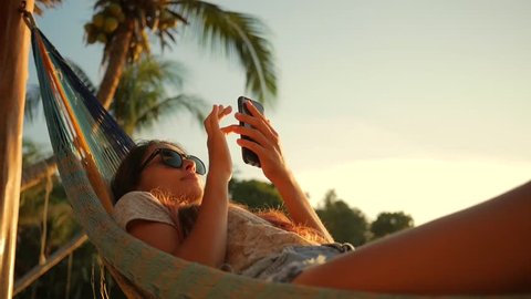 Relaxed Mixed Race Young Woman Looking at Mobile Phone in Hammock at the Beach near the Sea at Sunset. Koh Phangan, Thailand. HD Slowmotion. Stock Video