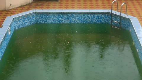 Heavy rain falls into a swimming pool. Not season, dirty abandoned pool