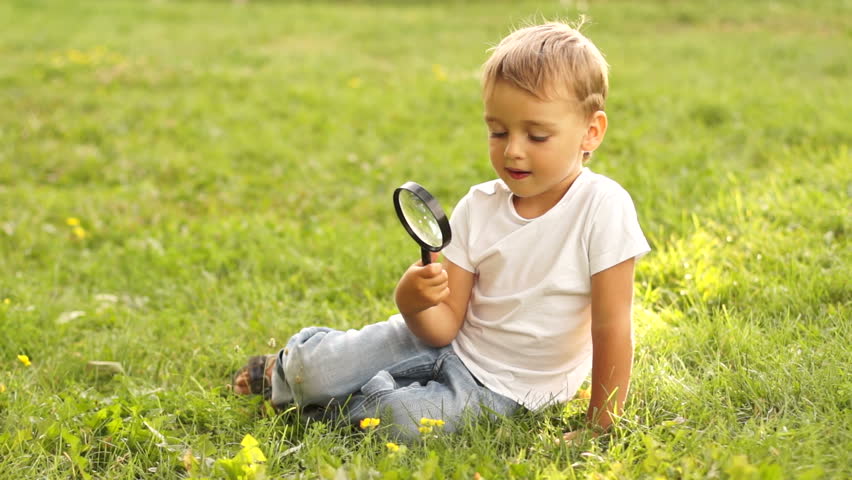 Boy with magnifier sitting on the grass
