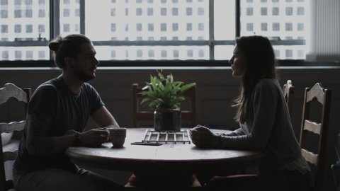 Young adult couple in loft apartment having coffee across table