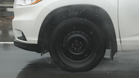 Slow motion drive. Passing vehicle. Detail of tire with droplets of water. Shot through rainy passenger window.
