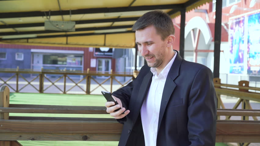 Smiling handsome man chatting on the smartphone on the street in sunny day 4K